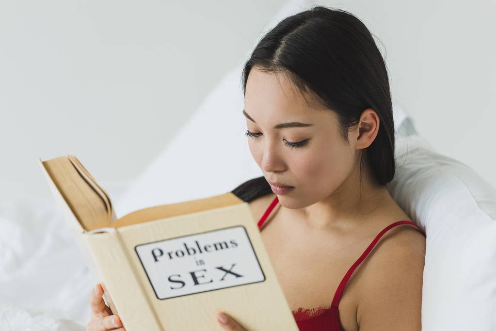 foco seletivo de mulher asiática concentrada leitura problemas no livro de sexo enquanto deitado na cama
 - Foto, Imagem