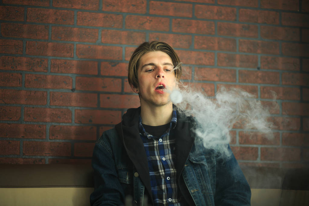 Adolescente de Vape. Retrato del joven guapo fumando un cigarrillo electrónico en el bar. Mal hábito que es perjudicial para la salud. Actividad de aspiración
. - Foto, imagen