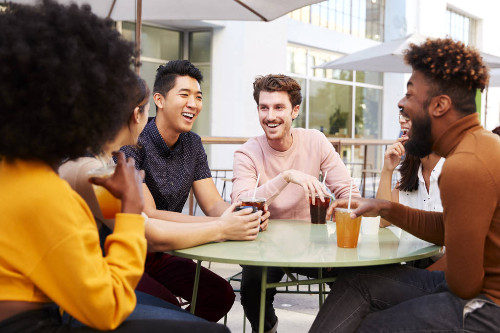 Six trendy millennial friends drinking cold brews and talking, sitting in the street outside a cafe - Photo, Image