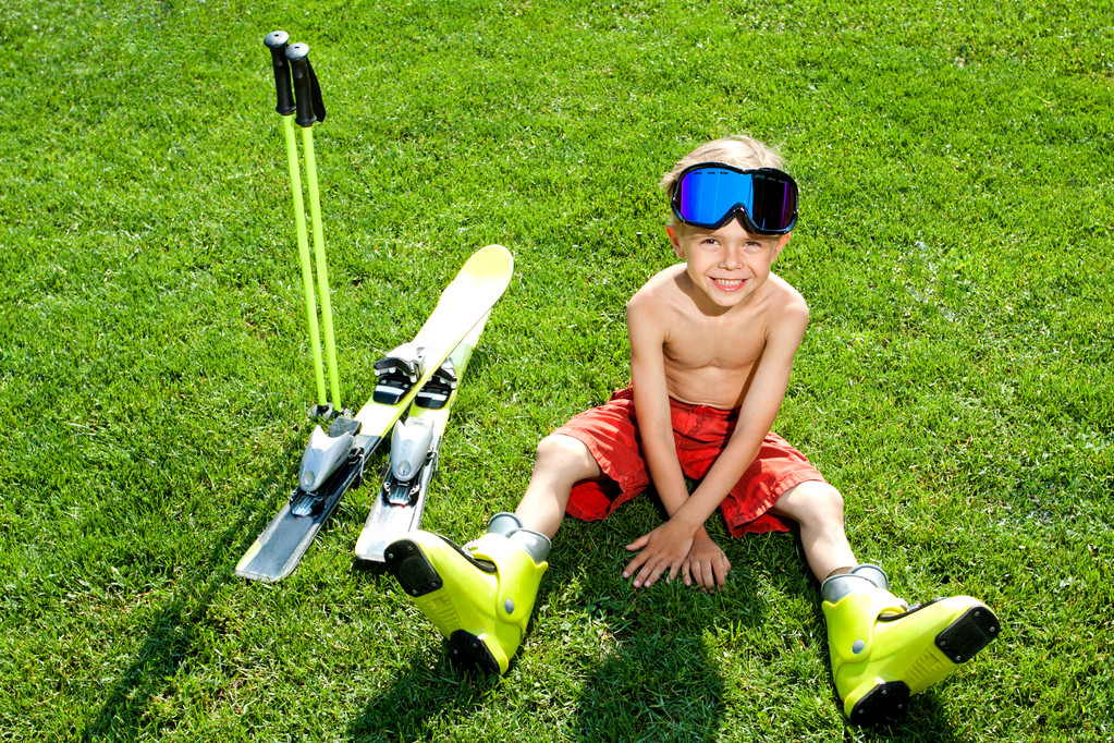Портрет привабливої дитини, що сидить на траві з лижами
 - Фото, зображення