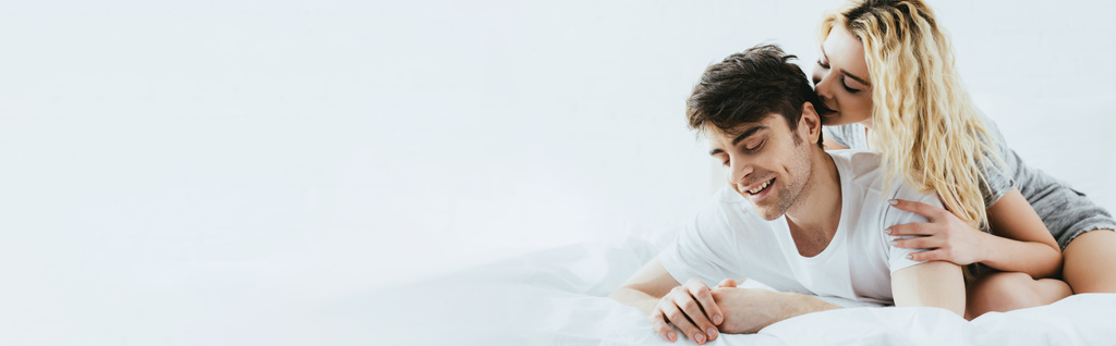 tiro panorâmico de menina loira feliz abraçando namorado bonito deitado na cama
  - Foto, Imagem