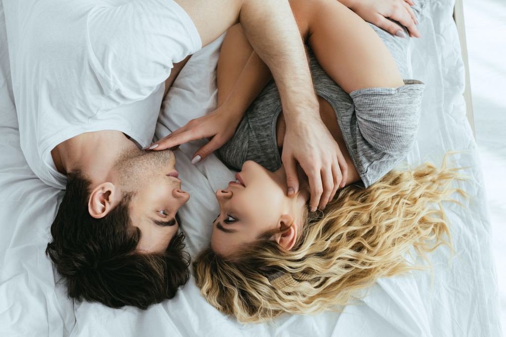 top view of blonde young woman touching face of boyfriend while  lying on bed  - Photo, Image