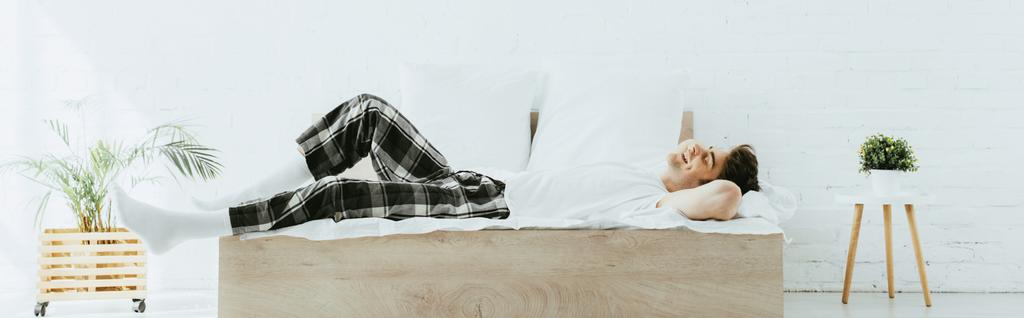 πανοραμική βολή του ευτυχισμένο άνθρωπο που βρίσκεται στο κρεβάτι στο μοντέρνο υπνοδωμάτιο  - Φωτογραφία, εικόνα
