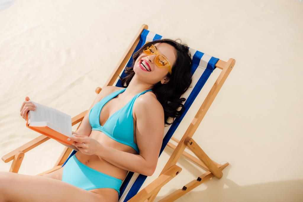 beautiful happy in girl bikini lying on deck chair with book on beach  - Photo, Image