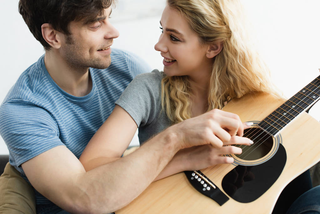 happy man and cheerful blonde woman holding hands of strings and looking at each other  - Photo, Image