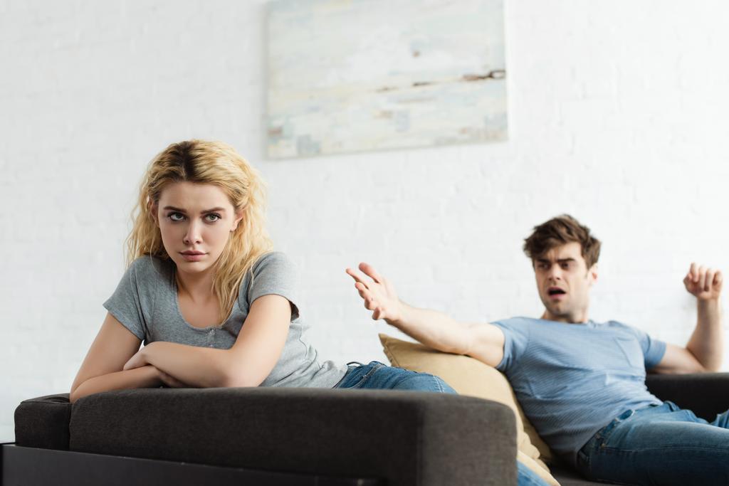 enfoque selectivo de mujer rubia frustrada con brazos cruzados cerca de hombre gesto en la sala de estar
  - Foto, imagen