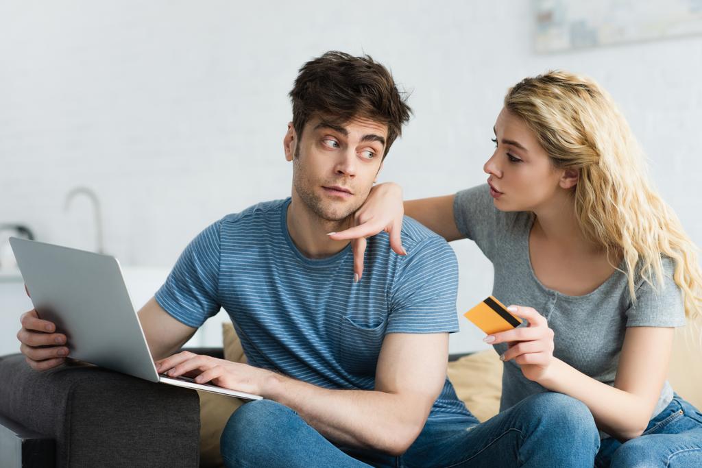 blonde woman pointing with finger at laptop laptop near man holding credit card  - Photo, Image