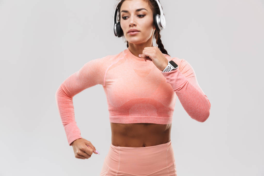 Increíble mujer de fitness deportivo fuerte posando aislado sobre fondo de pared blanca escuchando música con auriculares
. - Foto, Imagen