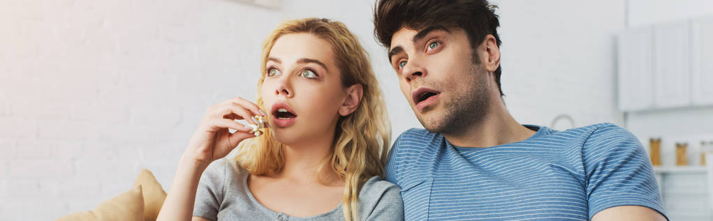 panoramische foto van geschokt man kijken naar film in de buurt van blonde meisje houden popcorn  - Foto, afbeelding