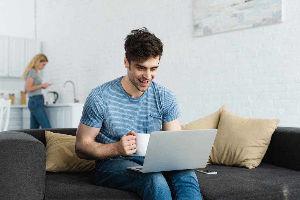 foyer sélectif de gai homme tenant tasse et regardant ordinateur portable près de la femme
  - Photo, image