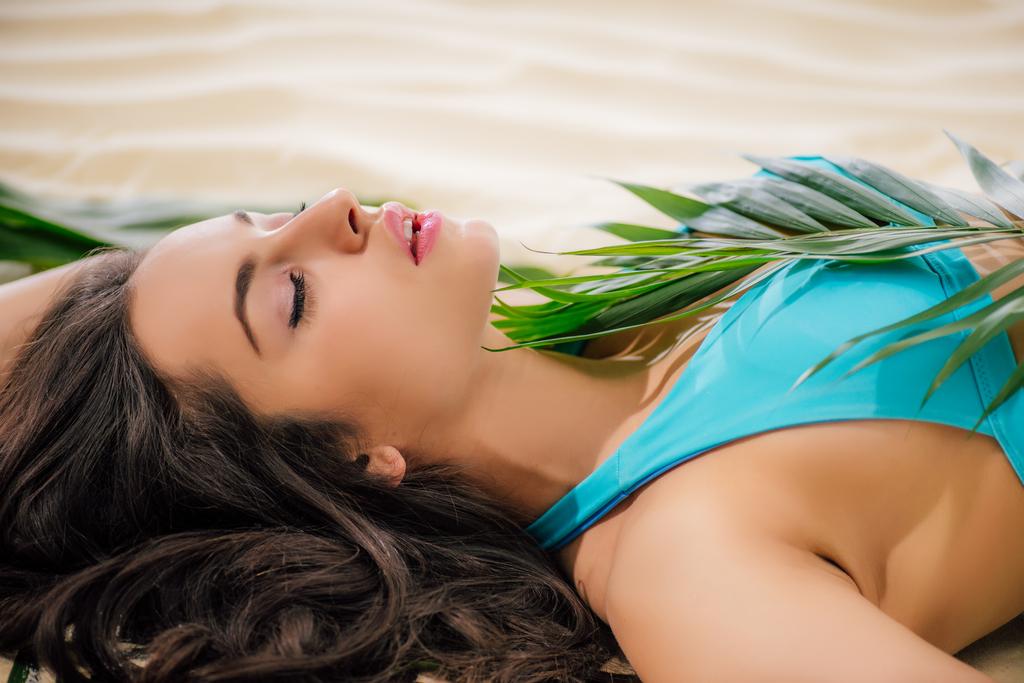 schönes Mädchen mit geschlossenen Augen posiert am Strand mit grünem Blatt - Foto, Bild