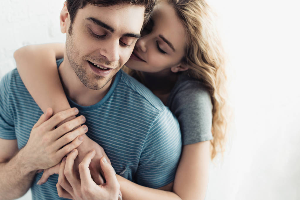 glückliche blonde Freundin umarmt gutaussehenden Mann mit geschlossenen Augen - Foto, Bild