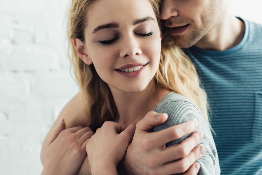 cropped view of man hugging happy blonde girl with closed eyes - Photo, Image