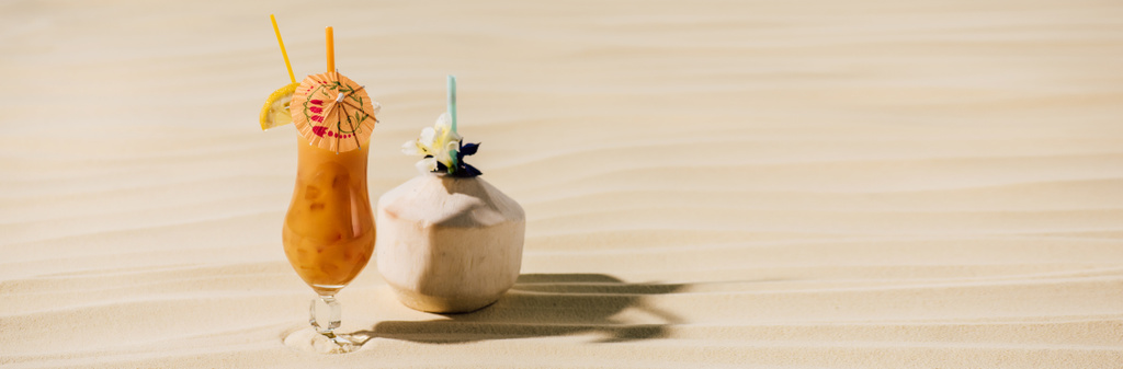 panoramisch shot van cocktail in kokos met bloem en cocktail in glas op zandstrand met Kopieer ruimte - Foto, afbeelding