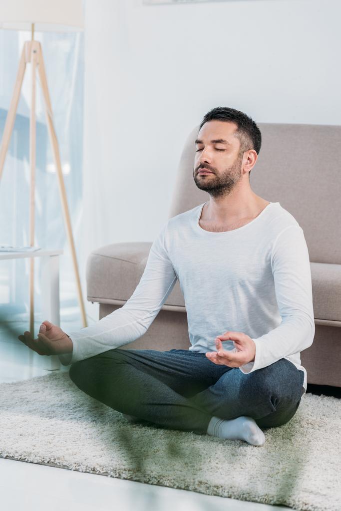 valikoiva painopiste komea mies istuu matolla Lotus Pose ja meditointi kotona
 - Valokuva, kuva