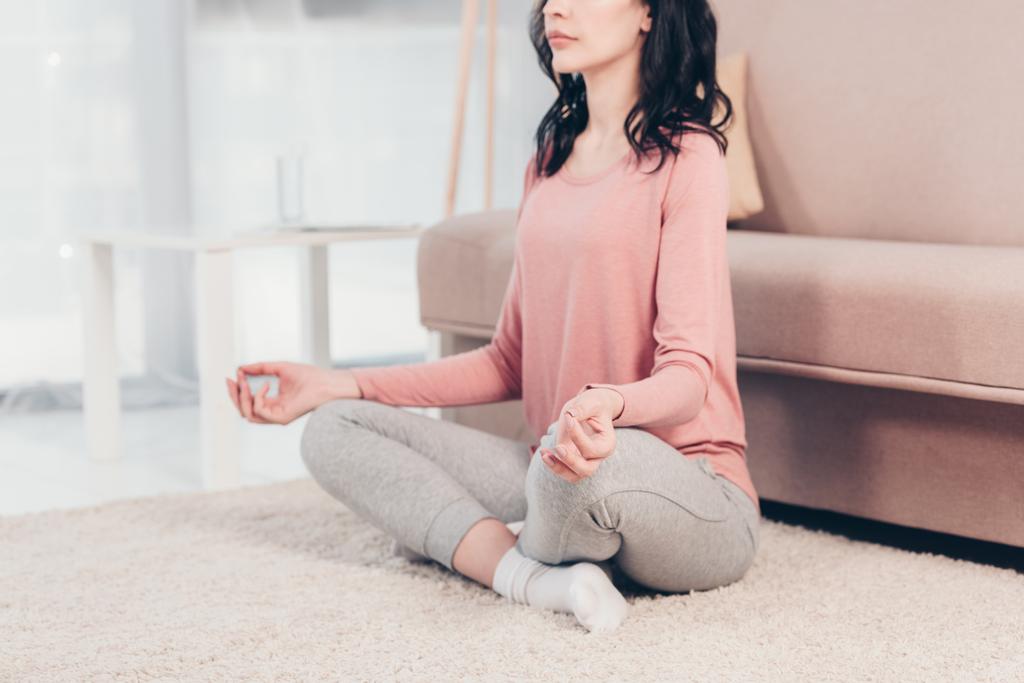 abgeschnittene Ansicht einer Frau in Lotuspose, die zu Hause im Wohnzimmer Meditation praktiziert - Foto, Bild