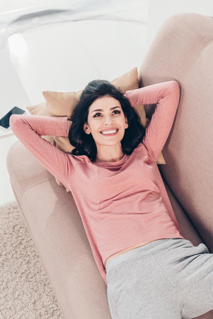 όμορφη ευτυχισμένη γυναίκα που αναπαύεται στον καναπέ με τα χέρια πίσω από το κεφάλι στο σπίτι - Φωτογραφία, εικόνα