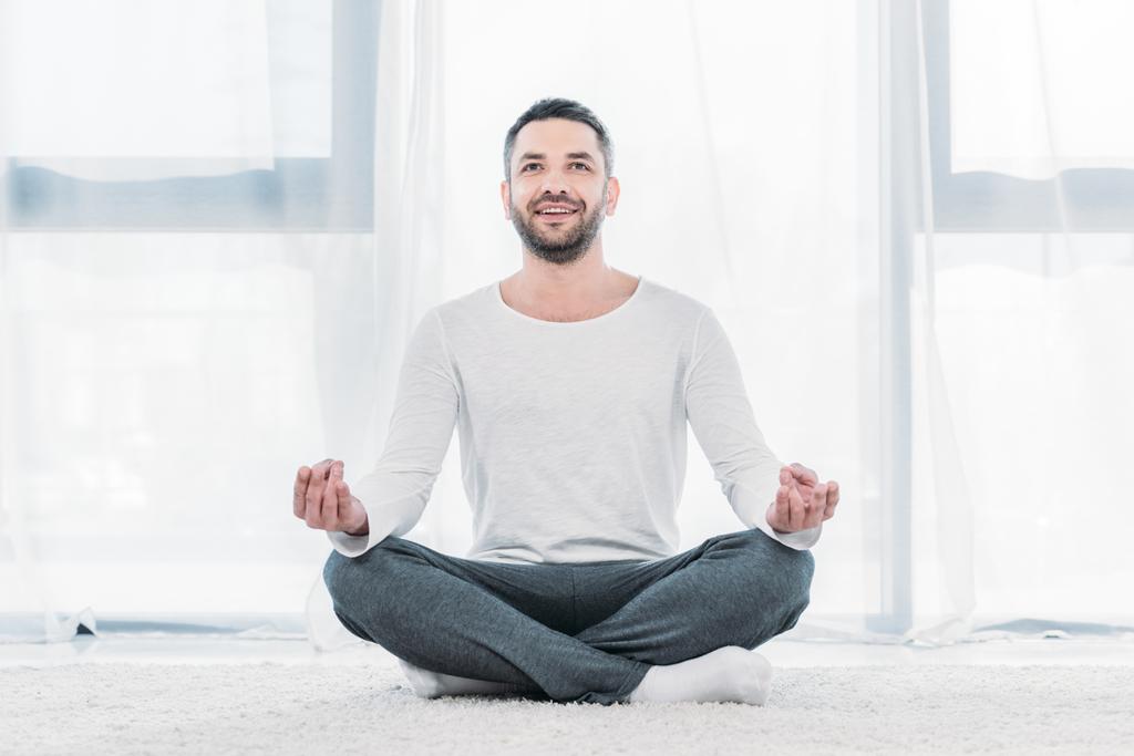 ロータスポーズでカーペットの上に座って、自宅で瞑想幸せなハンサムな男 - 写真・画像