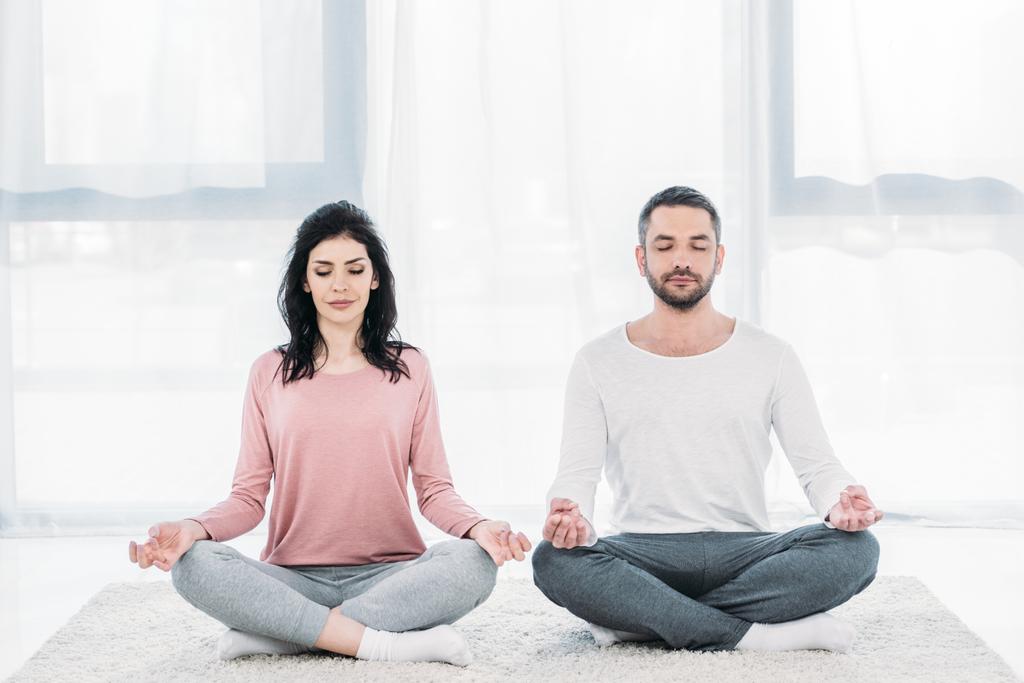vrouw en man met gesloten ogen zitten in Lotus Pose en mediteren thuis - Foto, afbeelding