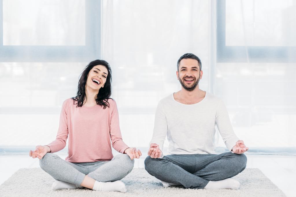 Gelukkige vrouw en man zitten in Lotus pose en mediteren thuis - Foto, afbeelding