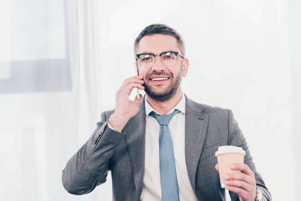 bell'uomo d'affari sorridente in occhiali e vestito con caffè per andare a parlare sullo smartphone
 - Foto, immagini