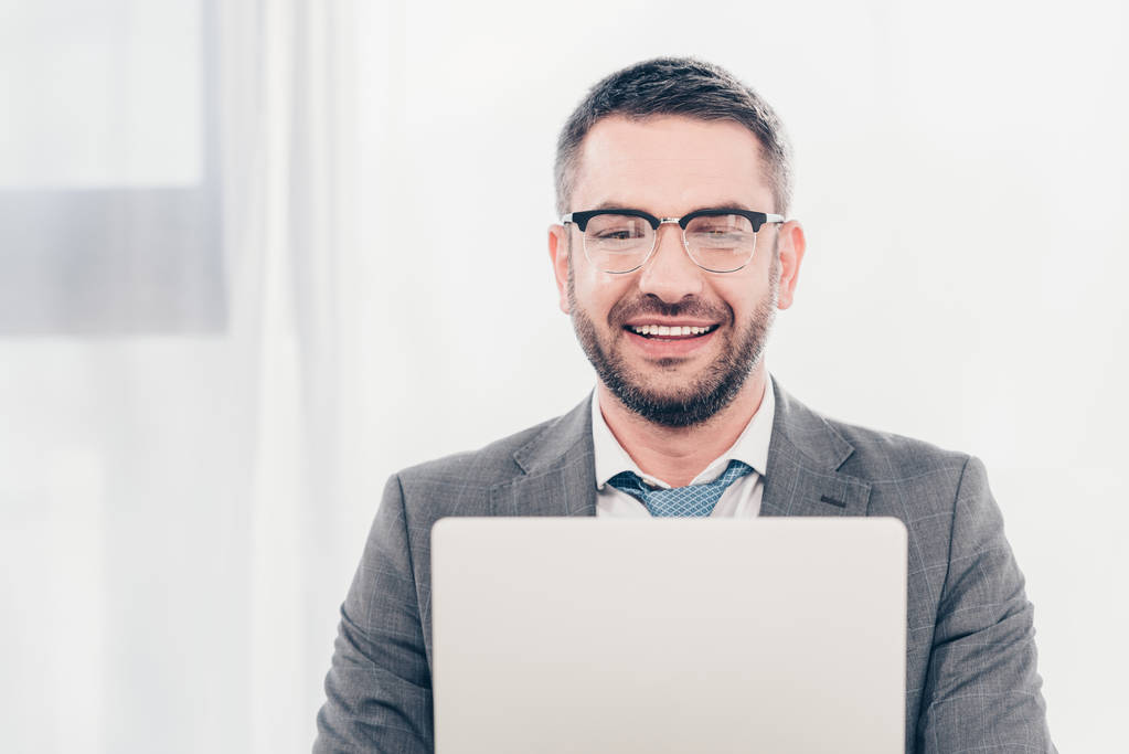 guapo hombre de negocios sonriente en gafas y traje usando el ordenador portátil
  - Foto, Imagen