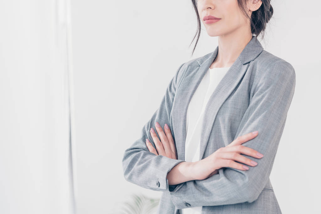 bijgesneden beeld van zakenvrouw in grijs pak met gekruiste armen op wit met Kopieer ruimte - Foto, afbeelding