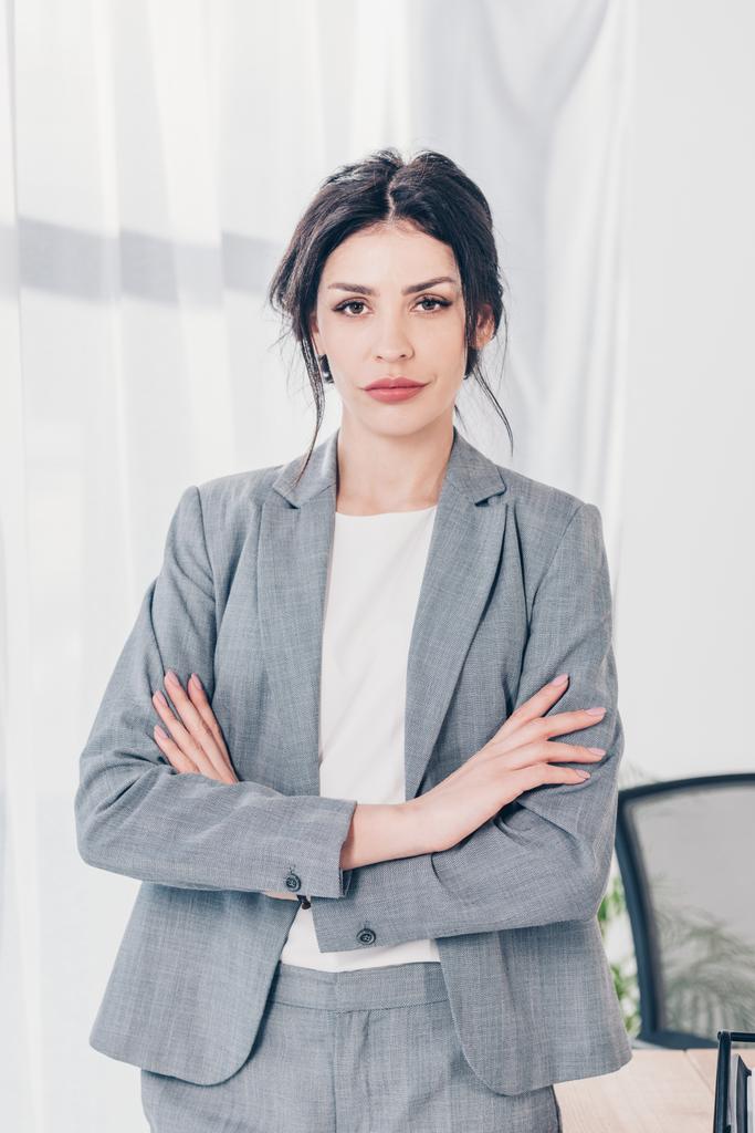 beautiful confident businesswoman in suit with crossed arms looking at camera in office - Photo, Image