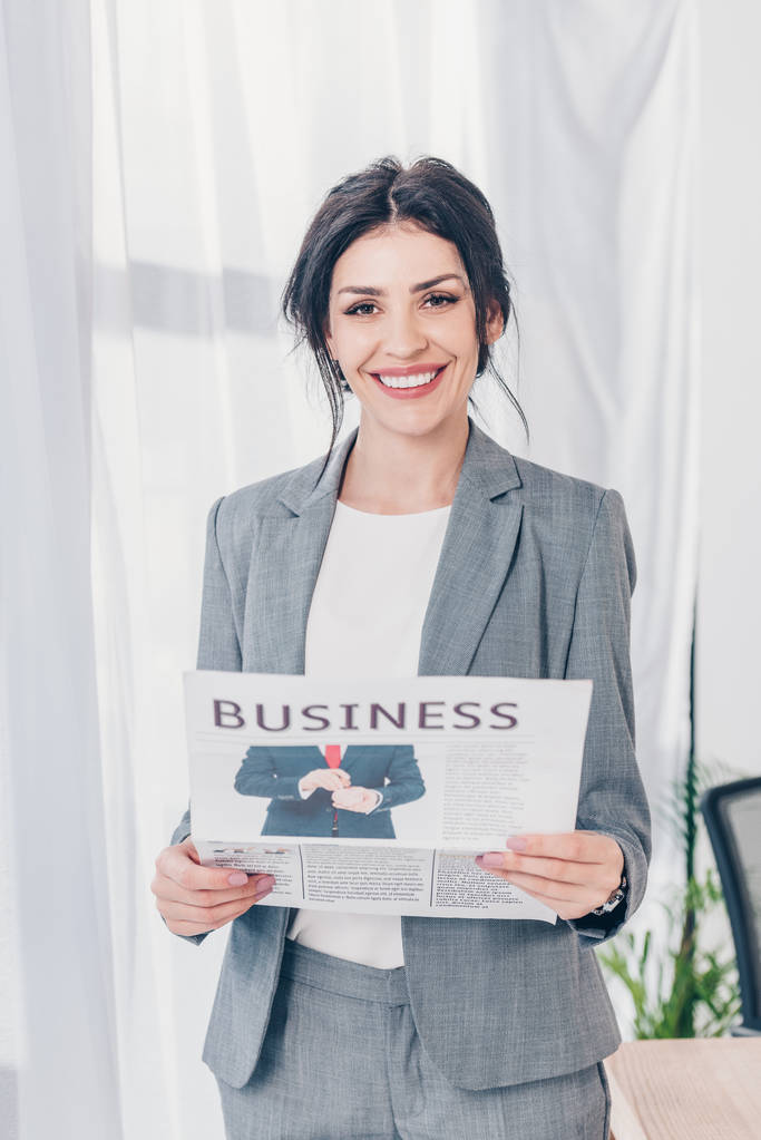 красивая деловая женщина в костюме держит газету и смотрит в камеру в офисе
  - Фото, изображение