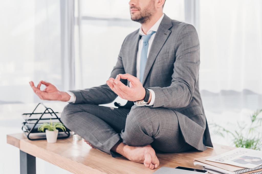 visão cortada de homem de negócios meditando em Lotus Pose na mesa de escritório
 - Foto, Imagem