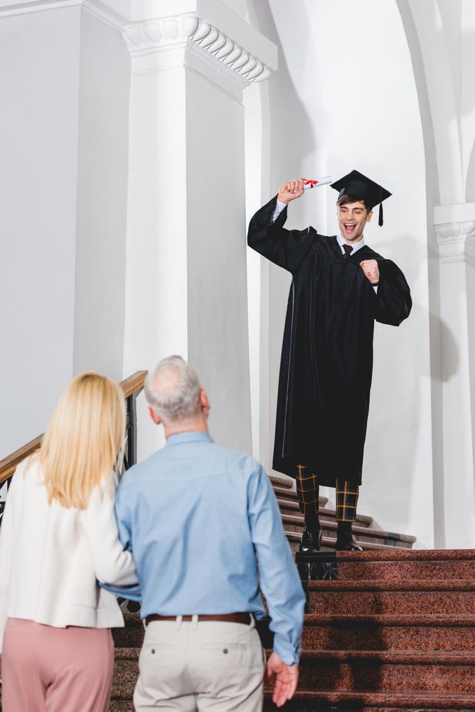 diploma tutarken mezuniyet kap gesturing mutlu oğlu bakarak ebeveynlerin geri görünümü  - Fotoğraf, Görsel