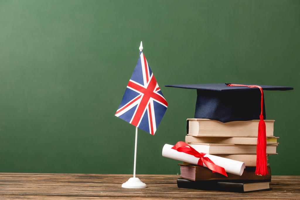 Knihy, akademická čepice, diplom a britská vlajka na dřevěné ploše izolované na zelené - Fotografie, Obrázek