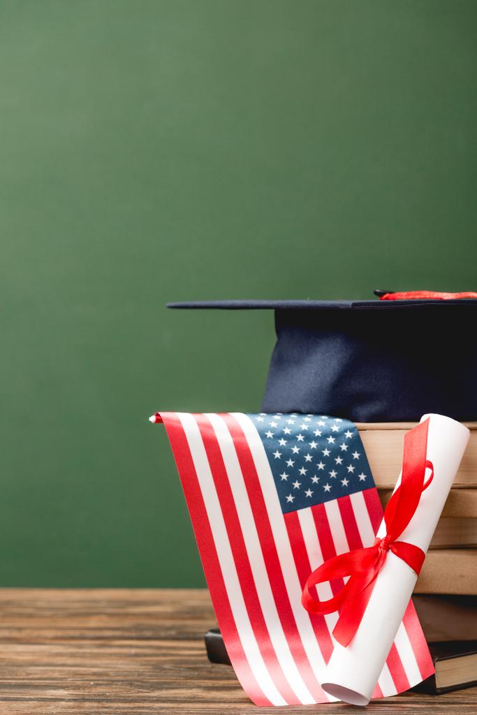 books, academic cap, diploma and american flag on wooden surface isolated on green - Photo, Image