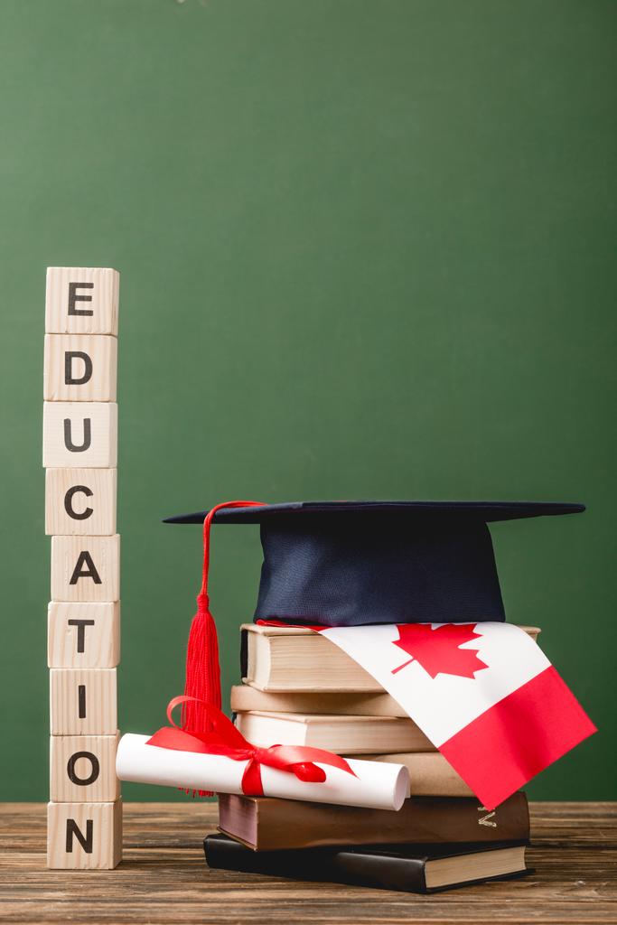 ξύλινα μπλοκ με γράμματα, ακαδημαϊκό καπάκι, βιβλία, δίπλωμα και καναδική σημαία σε ξύλινη επιφάνεια που απομονώνονται σε πράσινο - Φωτογραφία, εικόνα