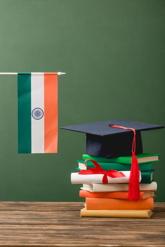 книги, диплом, академическая шапка и индийский флаг на деревянной поверхности изолированы на зеленом
 - Фото, изображение