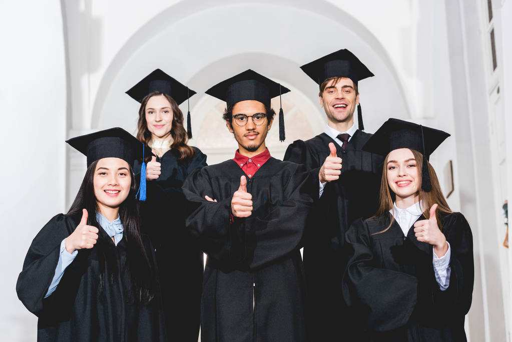 卒業式のガウンを着た陽気な学生が立ち上がり、親指を立て上げる - 写真・画像