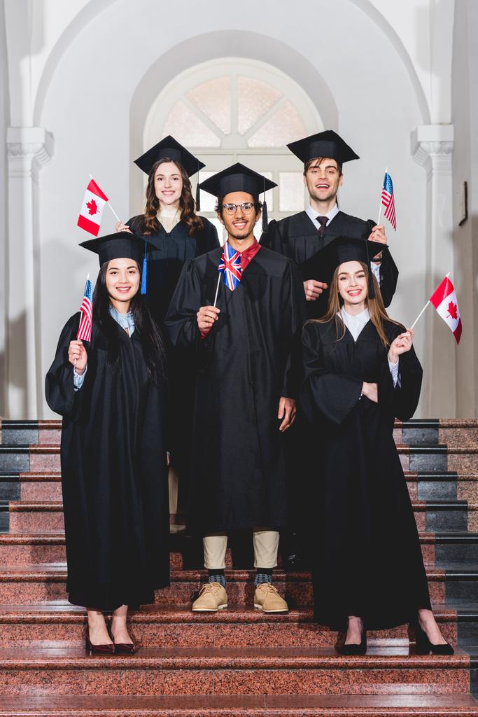 estudantes alegres em vestidos de graduação segurando bandeiras de diferentes países
   - Foto, Imagem