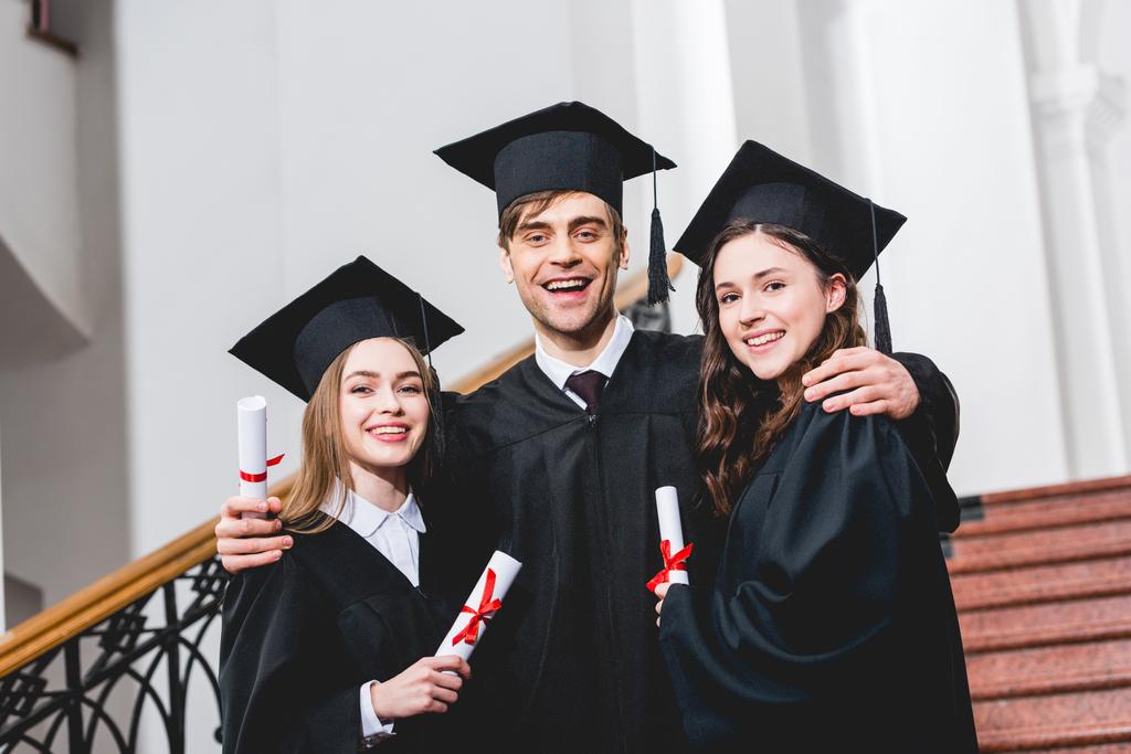 веселий чоловік у випускній шапці обіймає привабливих дівчат, тримаючи диплом
  - Фото, зображення