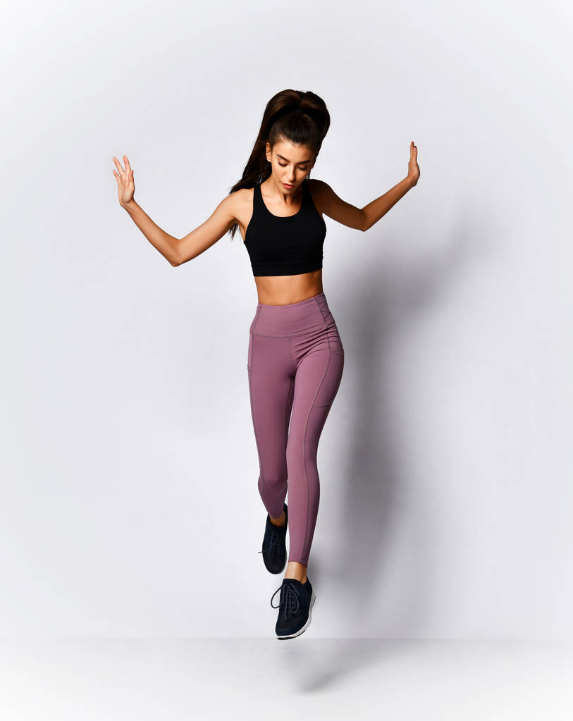 Slanke brunette vrouw Running Jumping doen workout oefening in sport slijtage op grijs  - Foto, afbeelding
