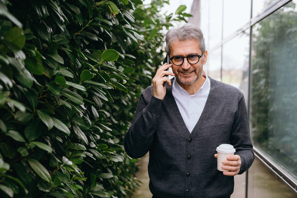 Człowiek spaceru na zewnątrz za pomocą telefonu komórkowego i picia kawy - Zdjęcie, obraz