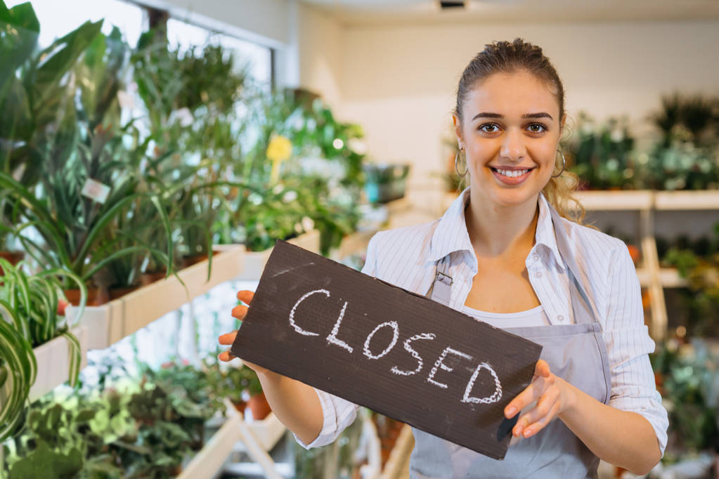Woman florist holding closed sign in flower shop - 写真・画像