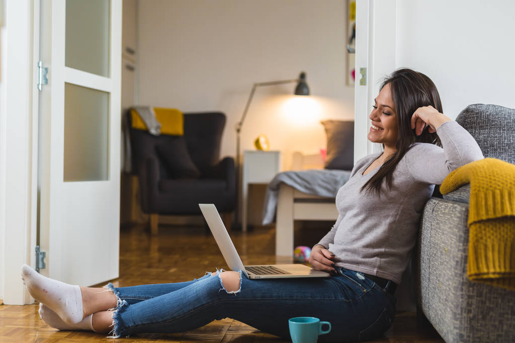 Mujer relajada usando laptop y tomando café en casa
 - Foto, Imagen