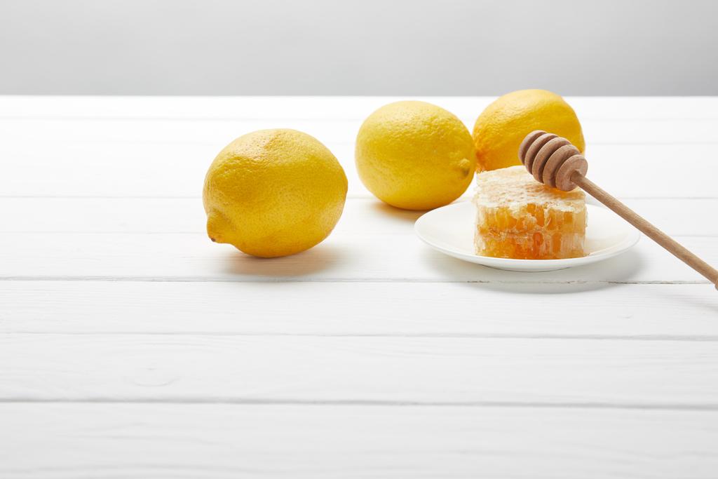 gri izole beyaz ahşap masa üzerinde lezzetli petek, limon ve bal damlatma - Fotoğraf, Görsel