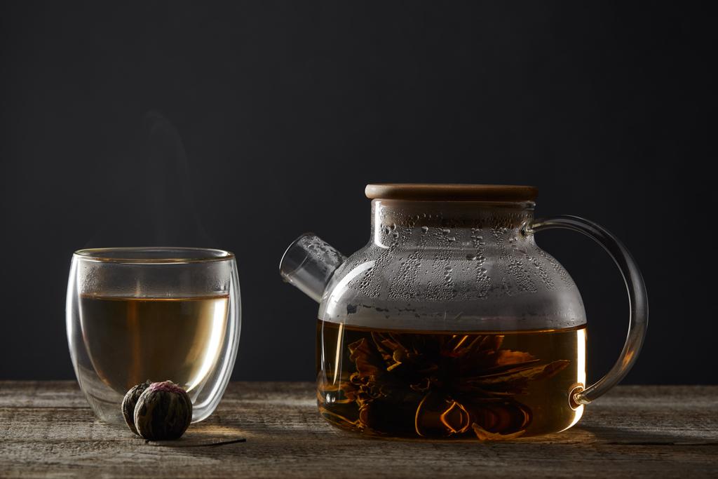 przezroczysta czajniczek i szklanka z kwitnącej herbaty na drewnianym stole na czarno - Zdjęcie, obraz