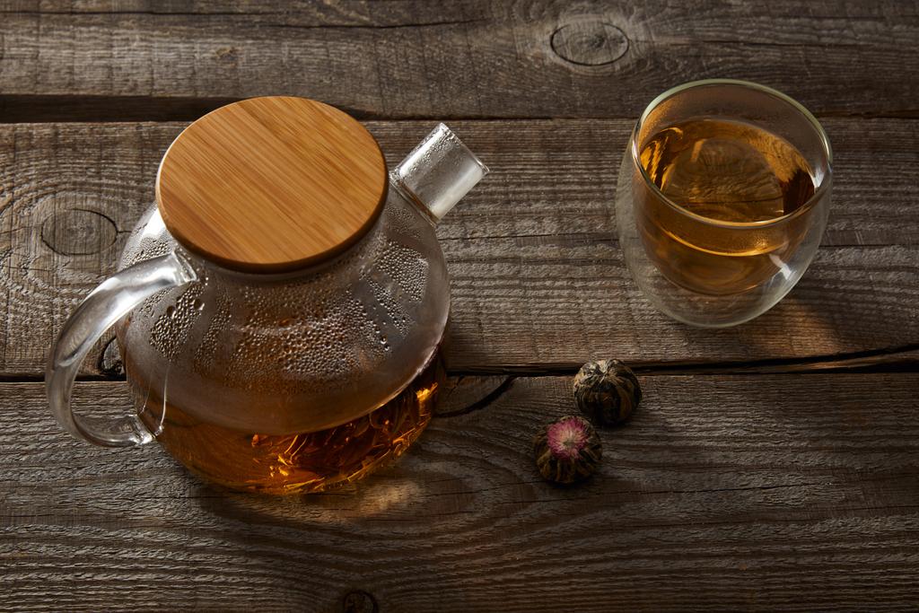 прозорий чайник і склянка з китайським квітучим чаєм на дерев'яному столі
 - Фото, зображення