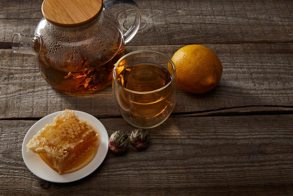 sitruuna, hunajakenno ja läpinäkyvä teekannu, jossa lasi kiinalaista kukkivaa teetä puupöydällä
 - Valokuva, kuva