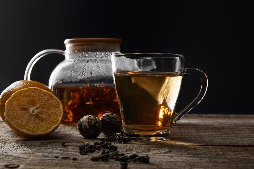 透明なティーポットとカップと伝統的な開花茶と黒に隔離されたレモンと木製のテーブルの上に - 写真・画像