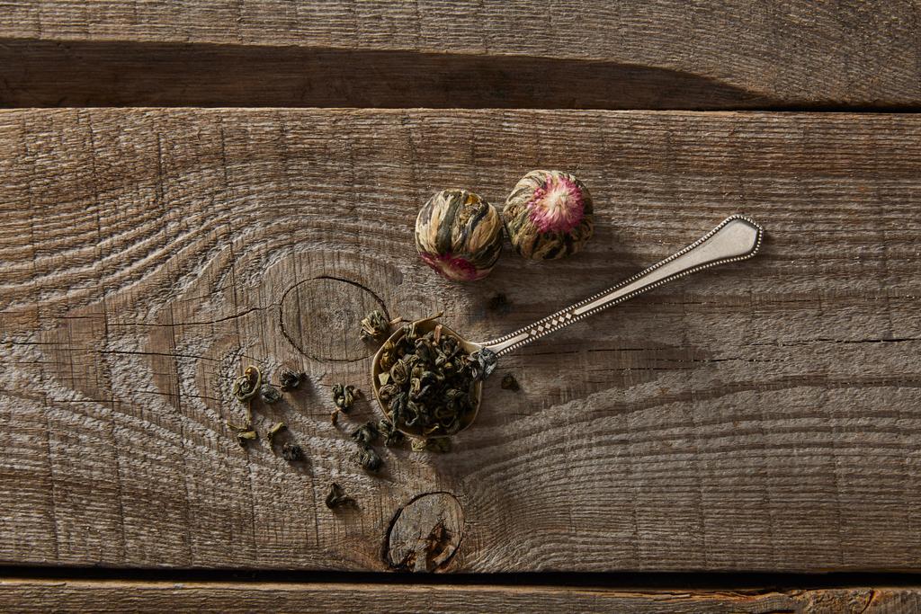 Κορυφαία θέα του κουταλιού με πράσινο τσάι και ανθισμένες μπάλες τσαγιού σε ξύλινο τραπέζι - Φωτογραφία, εικόνα