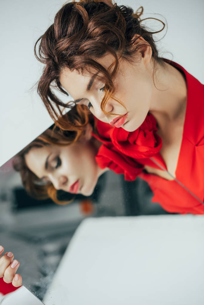 επιλεκτική εστίαση της ελκυστική κοκκινομάλλα νεαρή γυναίκα με κλειστά μάτια κρατώντας καθρέφτη σε λευκό - Φωτογραφία, εικόνα