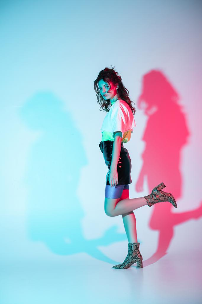 Atrakcyjna i stylowa kręcone młoda kobieta stoi na niebiesko z oświetleniem  - Zdjęcie, obraz